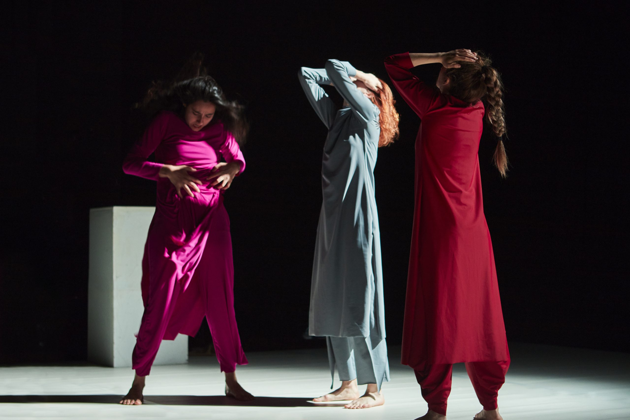 Tres mujeres en escena vestidas con unos vestidos de un color cada una. Las que van de rojo y azul miran hacia arriba y te tapan los ojos y la que viste de rosa se mira y toca la tripa