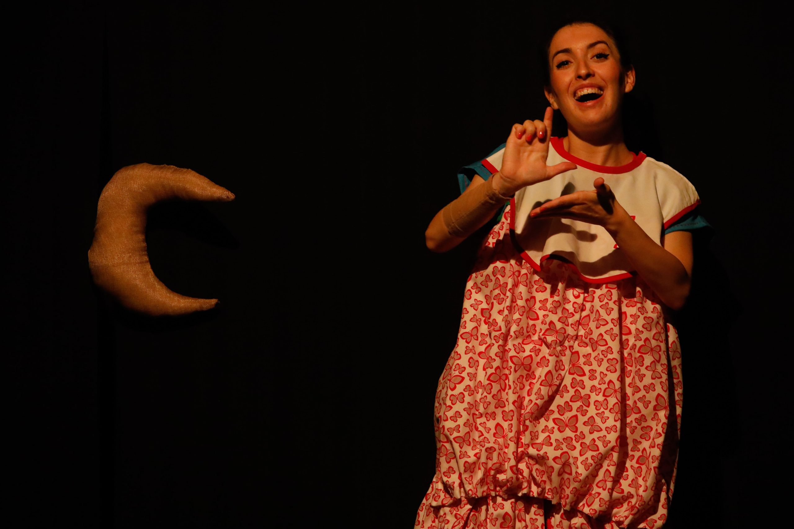 Una niña con un vestido rojo y blanco hablando en lengua de signos con una luna a su derecha