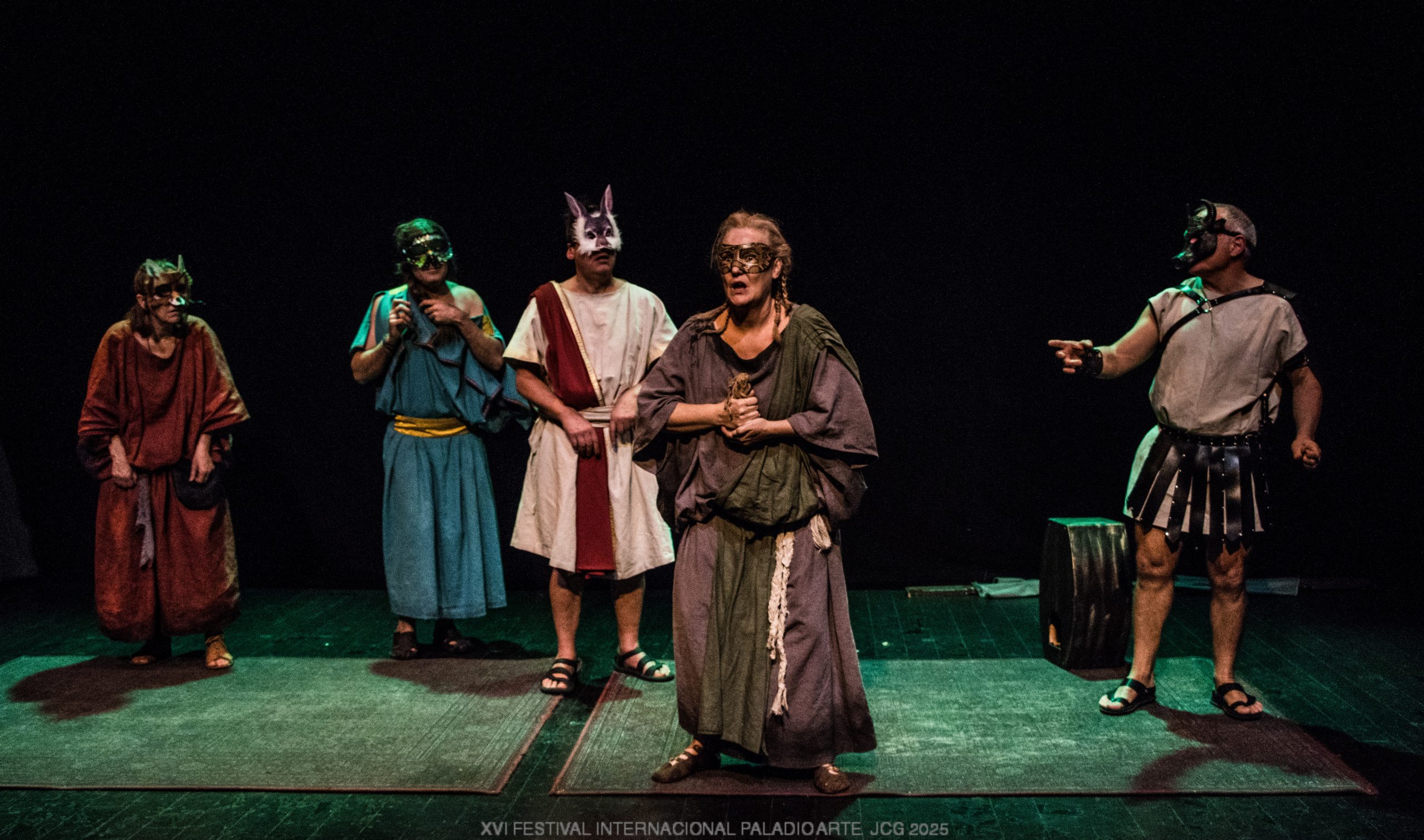 Foto de escena. Cinco personas con vestimentas estilo túnica de distintos colores. Cada una lleva una máscara de un animal.