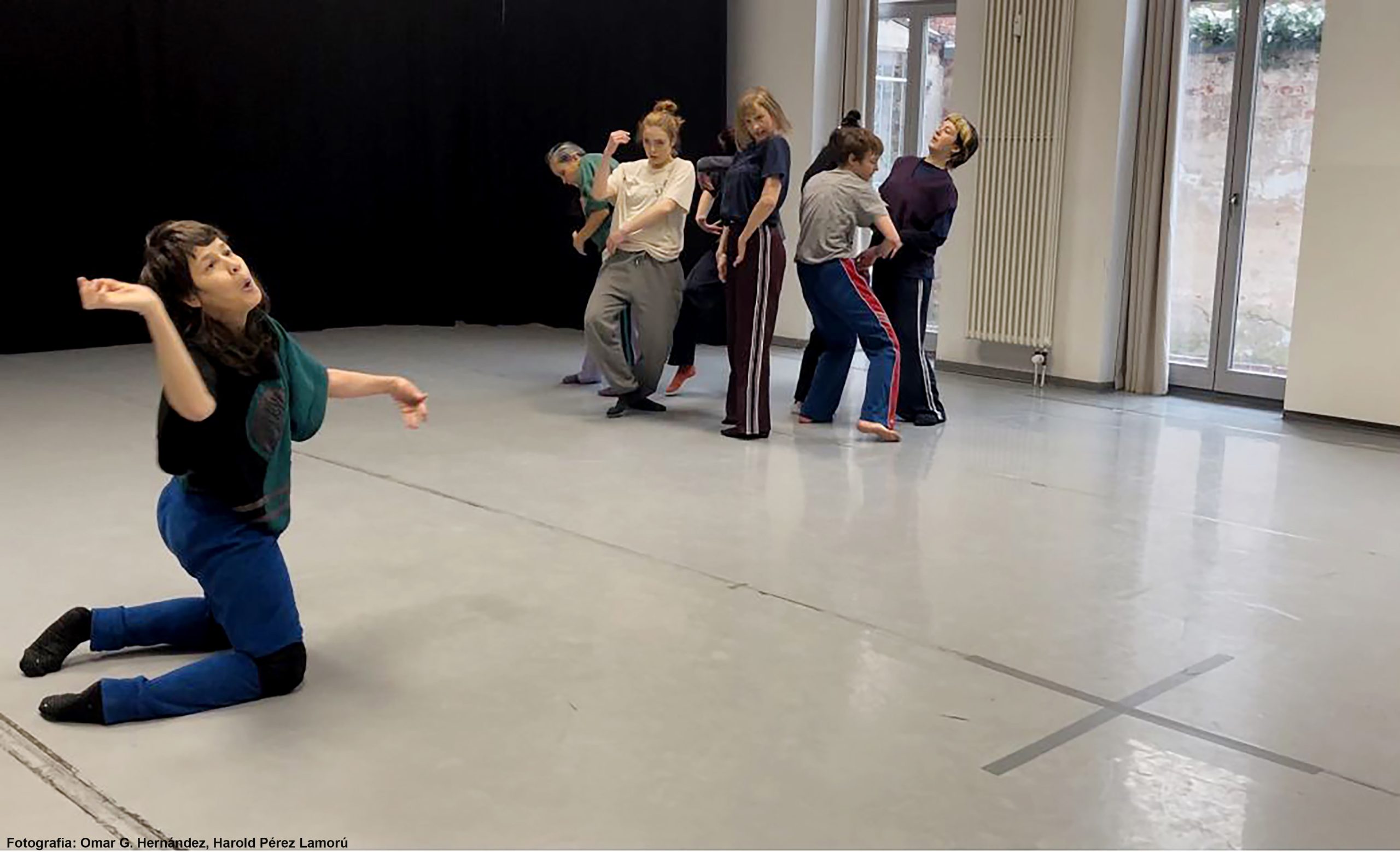 Foto del taller. Un grupo de personas se agrupan en un lado de la sala y en el otro lado la monitora da indicaciones